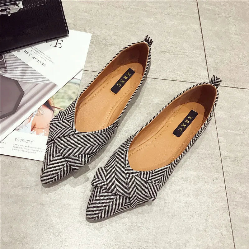 Women's black pointed toe slip-on shoes with a low flat heel on a plain background.