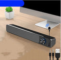 Compact black and white desktop computer speakers with USB cable on a wooden desk.