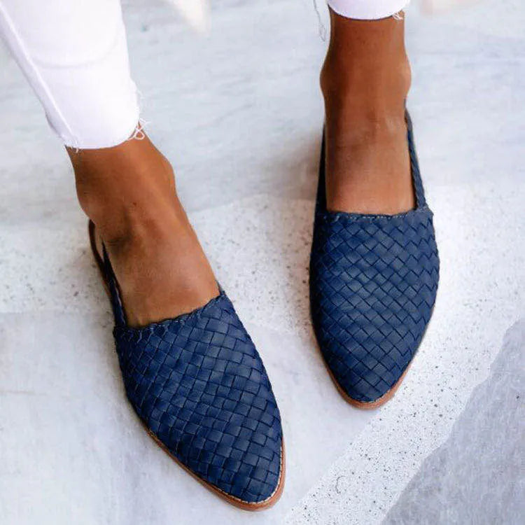 A pair of black baotou flat sandals with a buckle fastening and a pointed toe on a rubber sole.