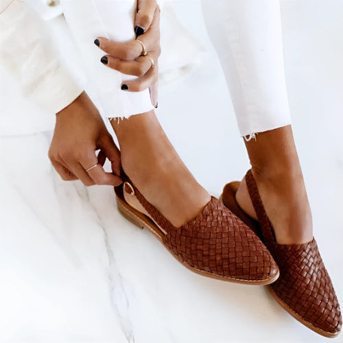 A pair of black baotou flat sandals with a buckle fastening and a pointed toe on a rubber sole.