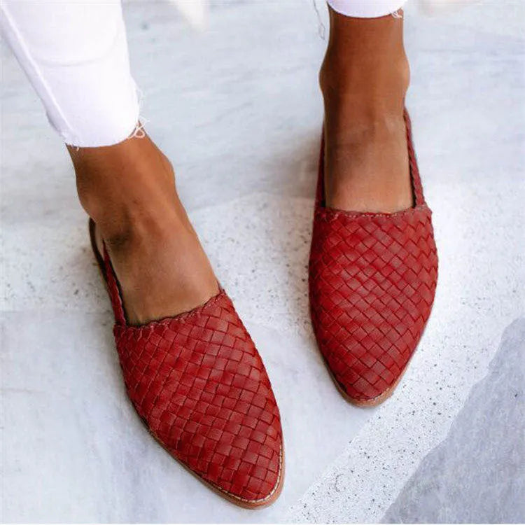 A pair of black baotou flat sandals with a buckle fastening and a pointed toe on a rubber sole.