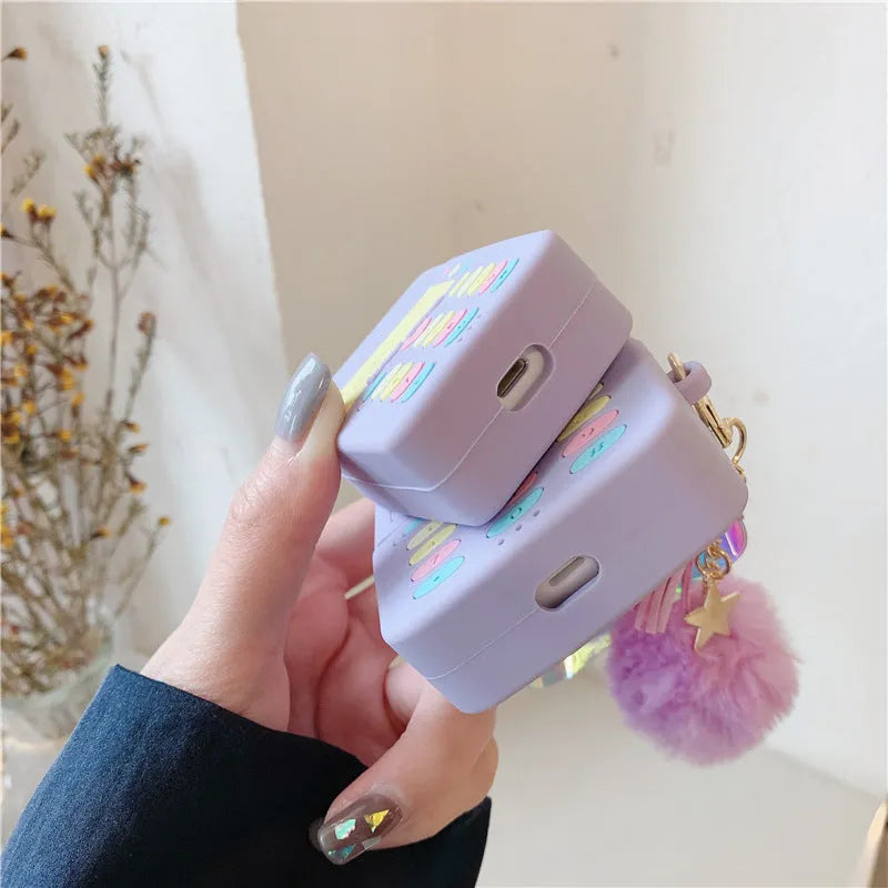 Purple silicone AirPods protective case with fur ball pendant attached to clamshell design