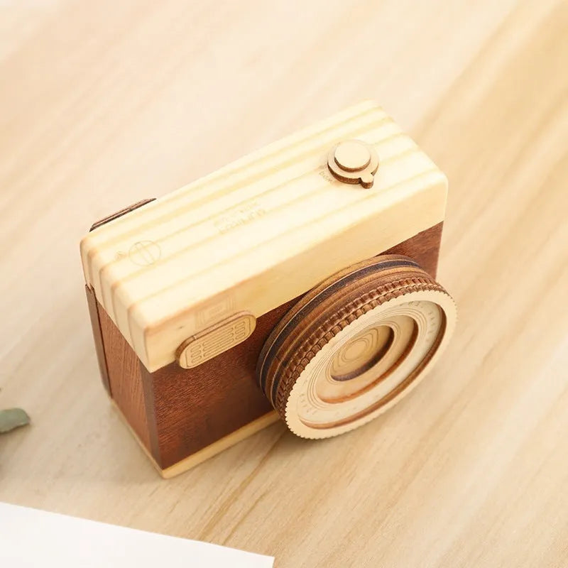 Wooden rotating camera music box in carton packaging, showing pine wood construction.