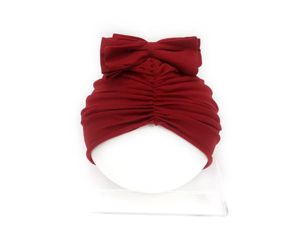 Baby girl wearing a soft, knitted purple turban-style hat on a white background.