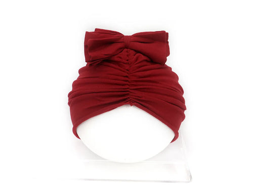 Baby girl wearing a soft, knitted purple turban-style hat on a white background.