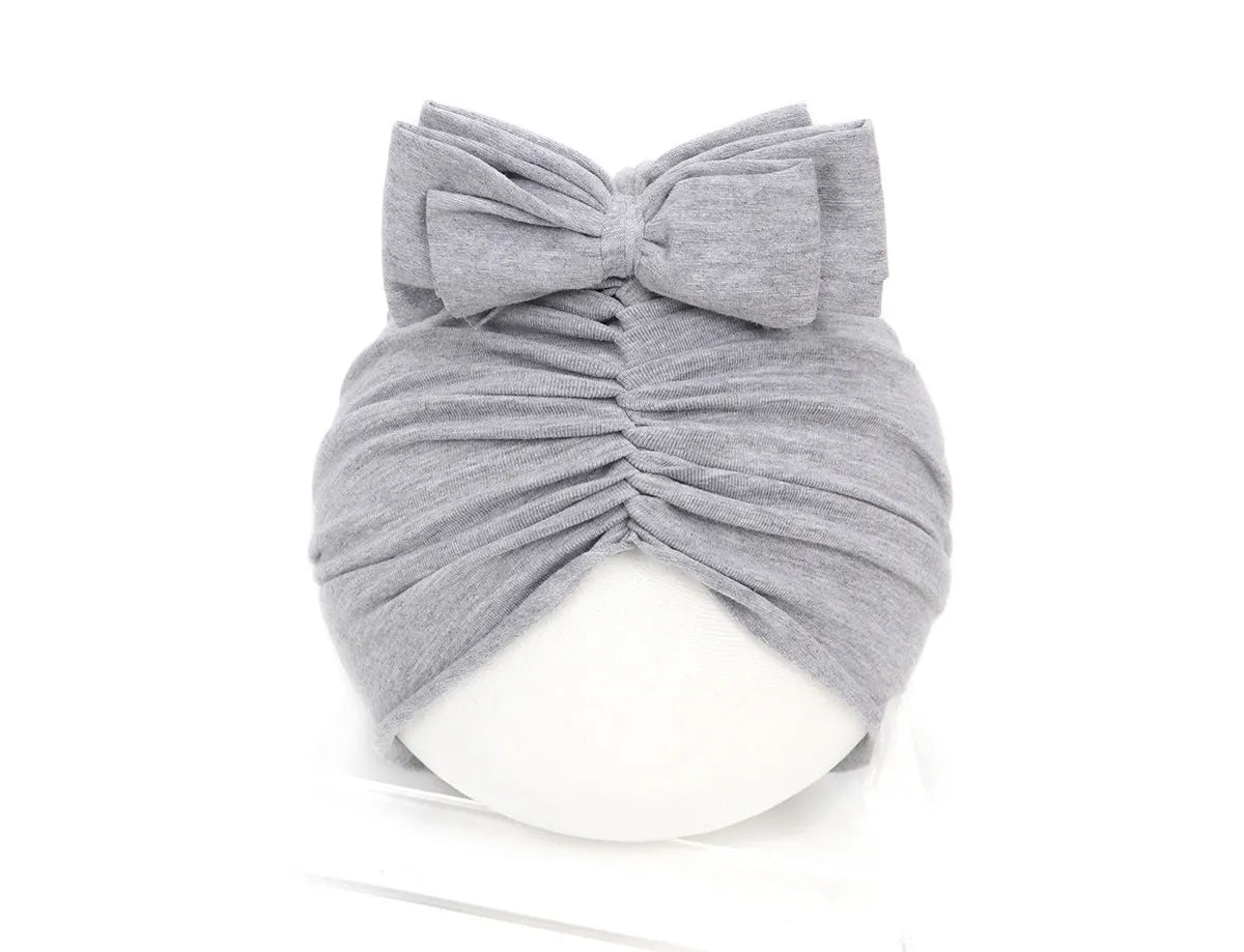 Baby girl wearing a soft, knitted purple turban-style hat on a white background.
