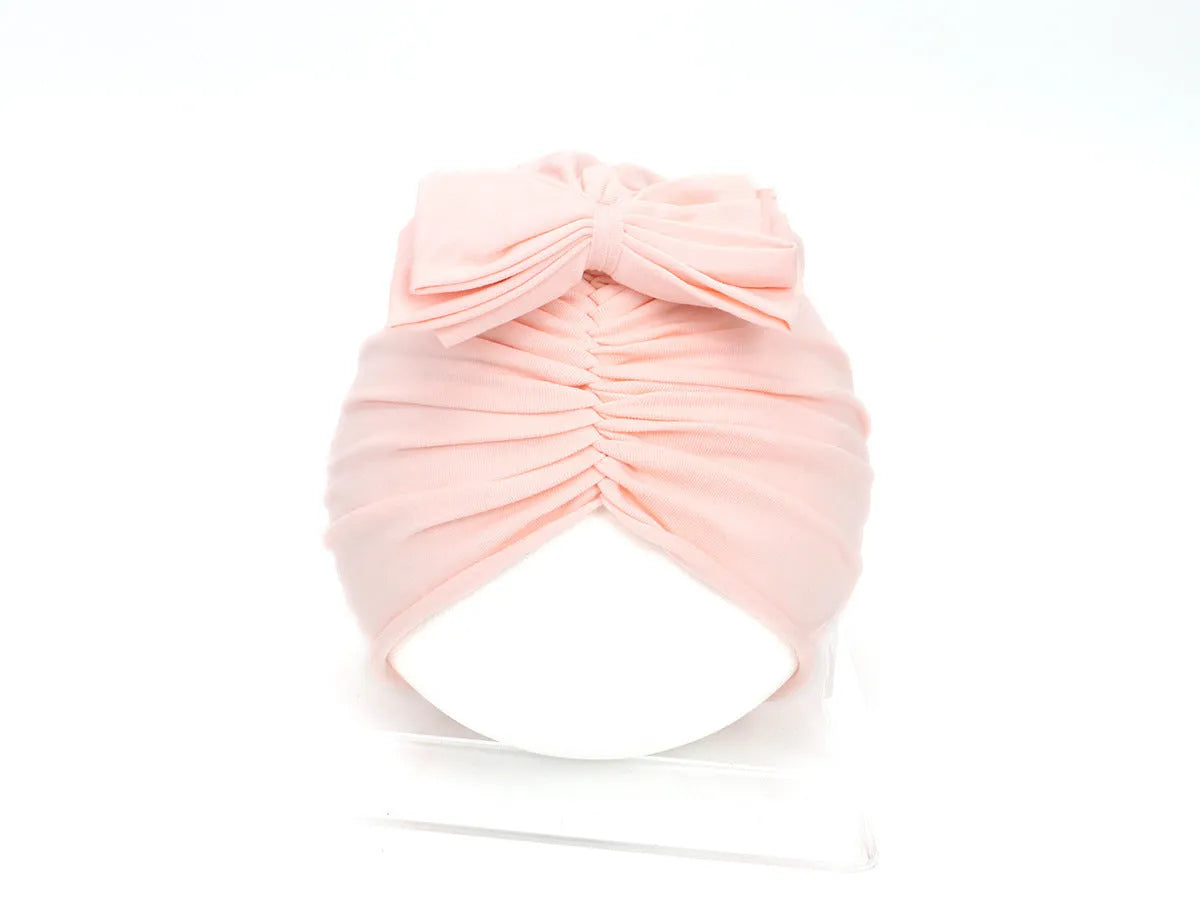 Baby girl wearing a soft, knitted purple turban-style hat on a white background.
