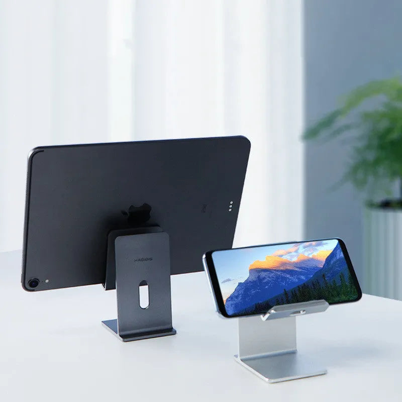 Dark Space Gray alloy mobile phone holder with a phone secured in its adjustable cradle on a wooden desk.
