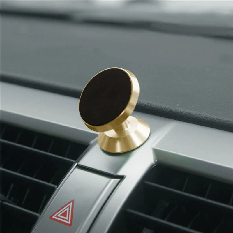 Universal magnetic car phone holder in black, silver, and gold colours on a car dashboard.