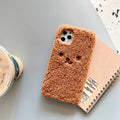 Brown embroidered plush bear face on a flexible TPU phone case for iPhone, showing camera cutout and raised edges.