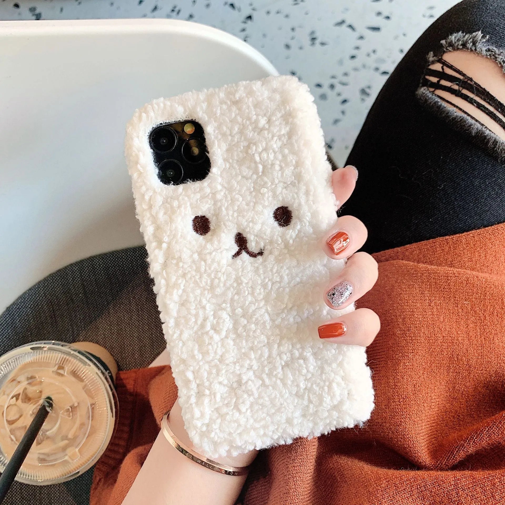 Brown embroidered plush bear face on a flexible TPU phone case for iPhone, showing camera cutout and raised edges.