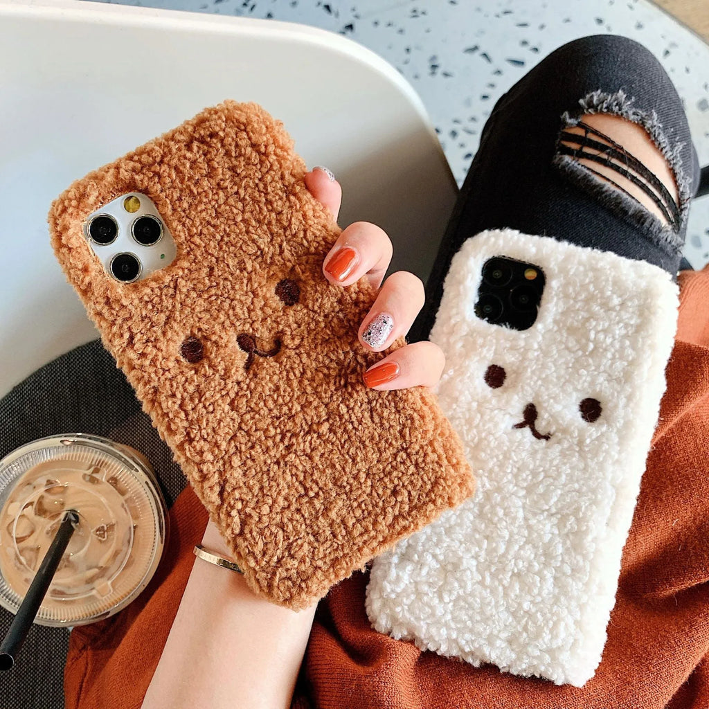 Brown embroidered plush bear face on a flexible TPU phone case for iPhone, showing camera cutout and raised edges.