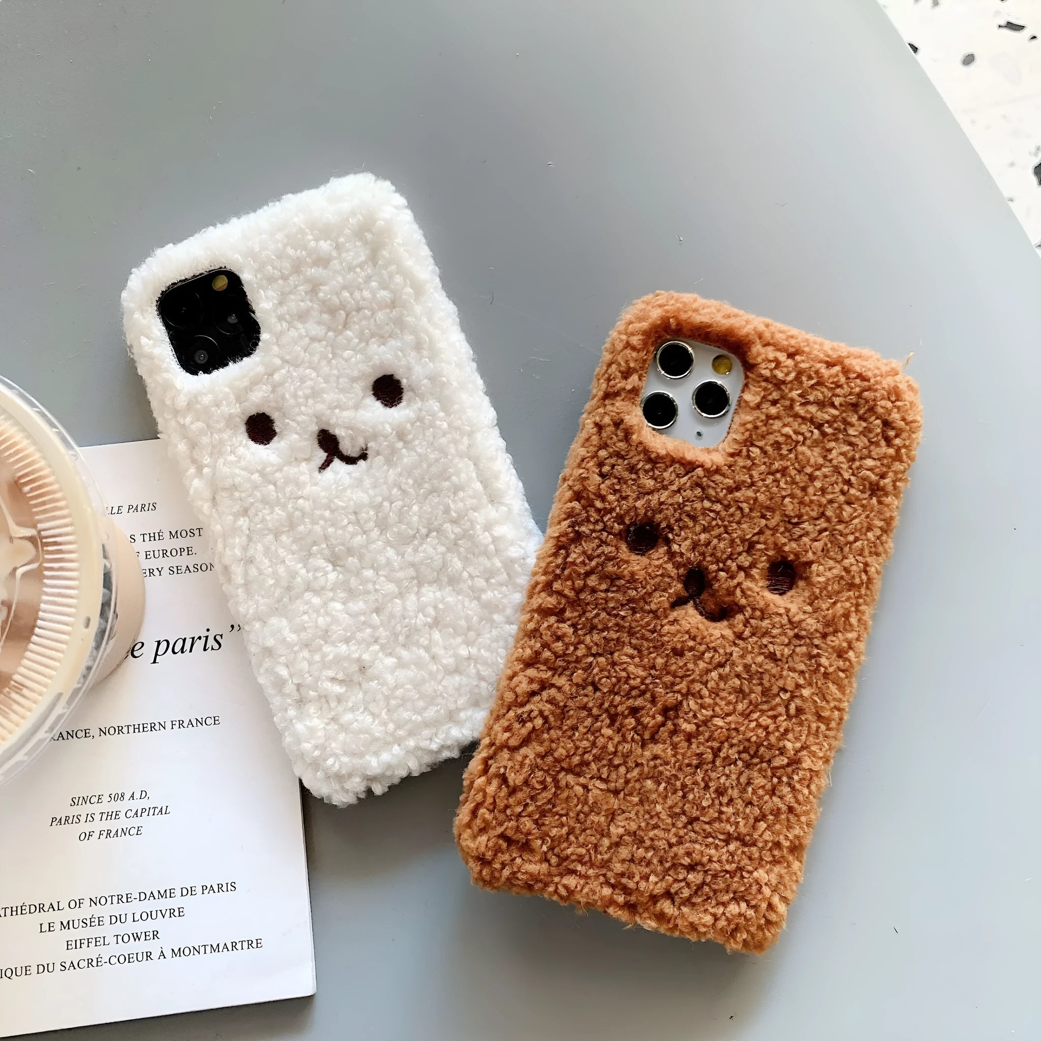 Brown embroidered plush bear face on a flexible TPU phone case for iPhone, showing camera cutout and raised edges.