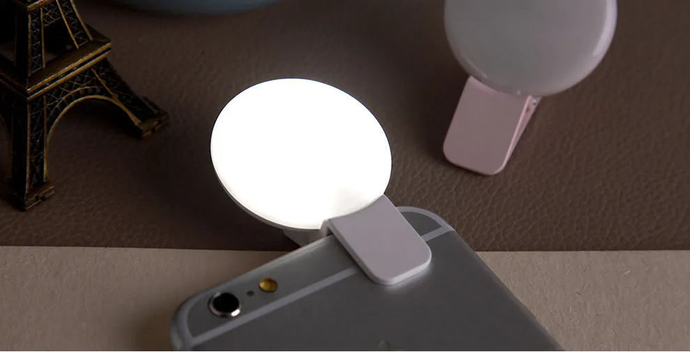 Round USB rechargeable LED fill light attached to a mobile phone for selfies.