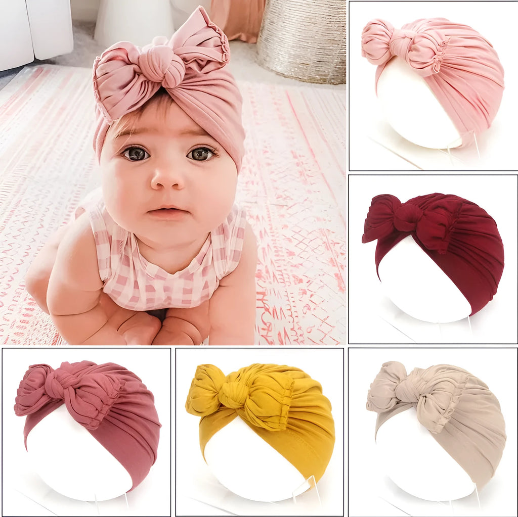 Baby girl wearing a soft, knitted purple turban-style hat on a white background.