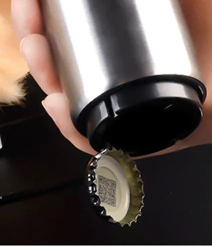 Stainless steel automatic bottle opener on a table, showing its compact size and press-down design.