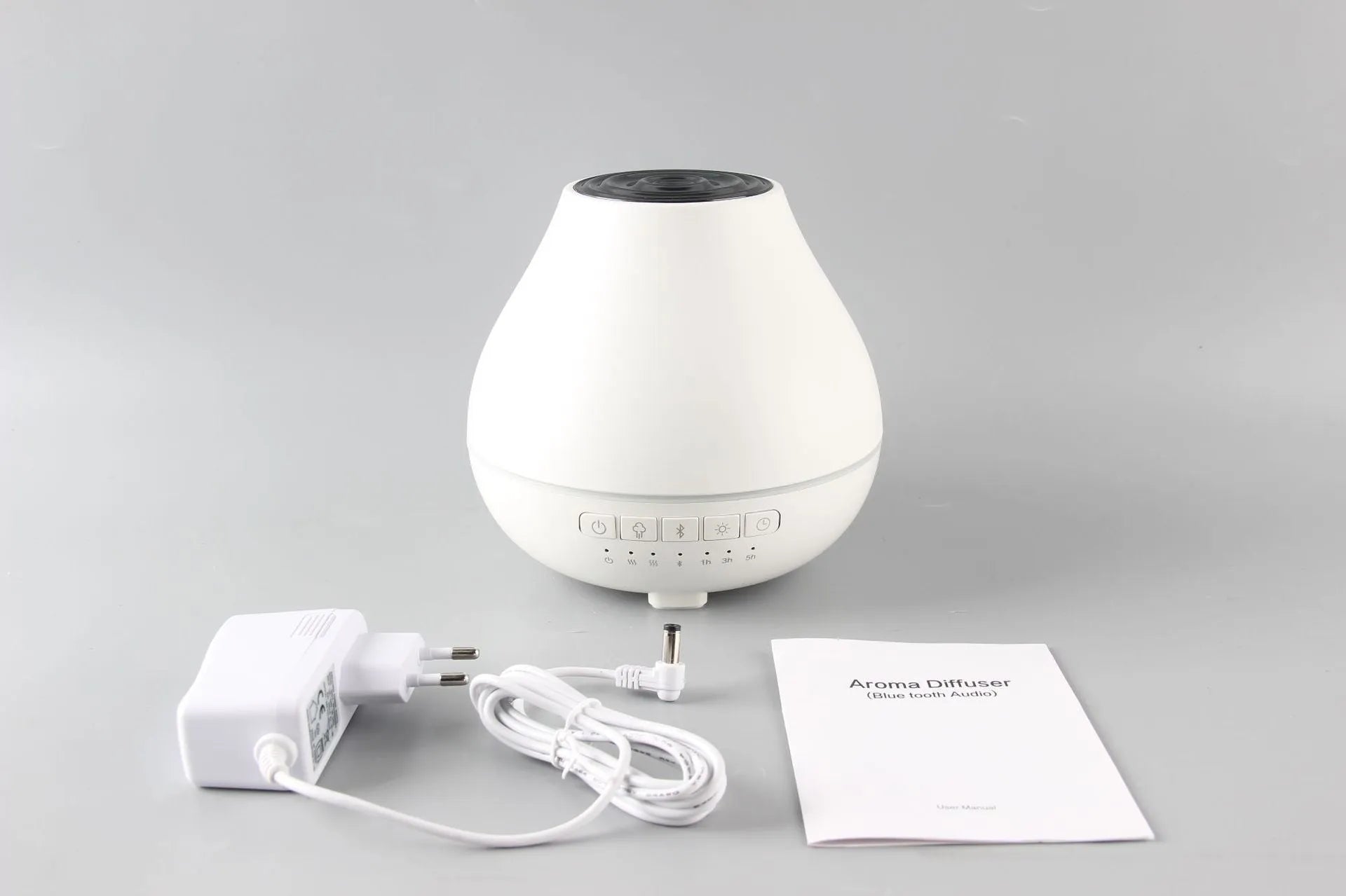 White round Bluetooth aroma diffuser with night light on wooden table, showing mist outlet and water tank.