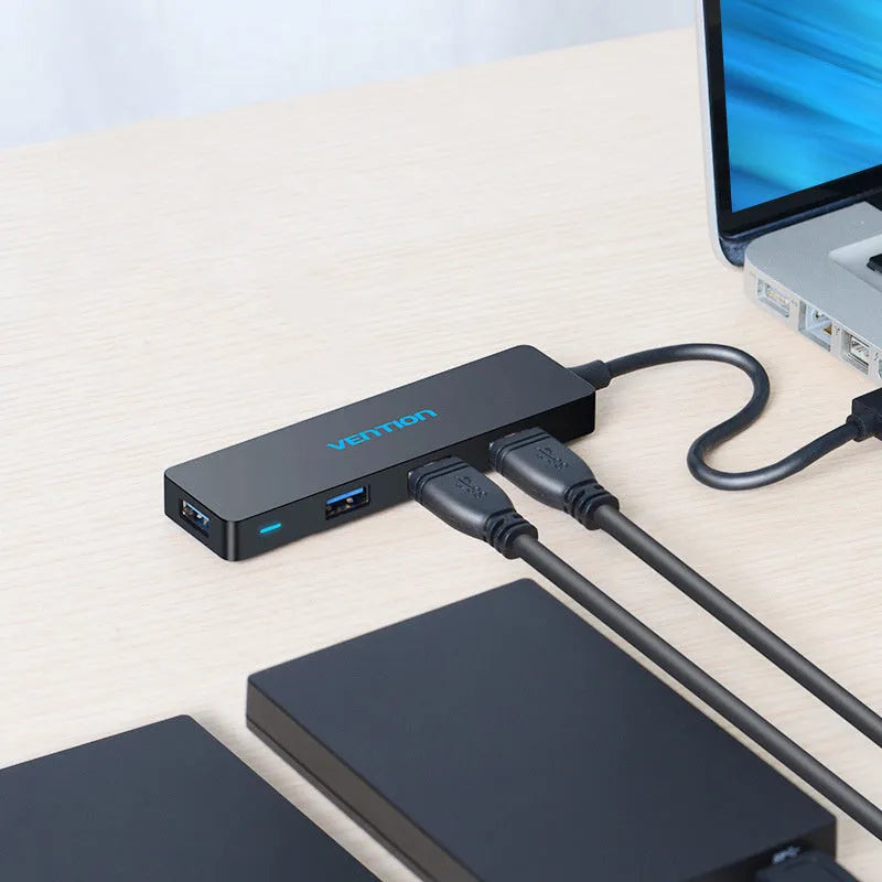 Black Wei Xun four-port USB 3.0 hub with short 15cm cable on a desk next to a laptop.