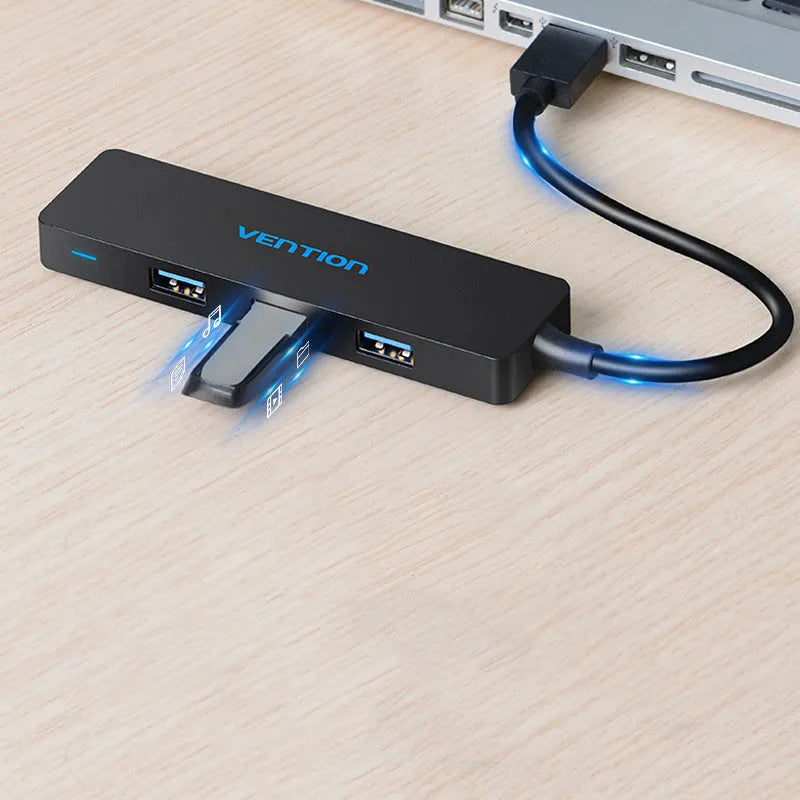 Black Wei Xun four-port USB 3.0 hub with short 15cm cable on a desk next to a laptop.