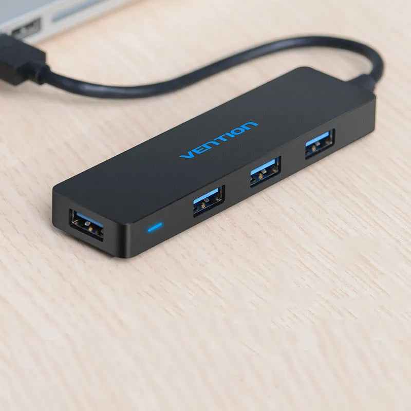 Black Wei Xun four-port USB 3.0 hub with short 15cm cable on a desk next to a laptop.