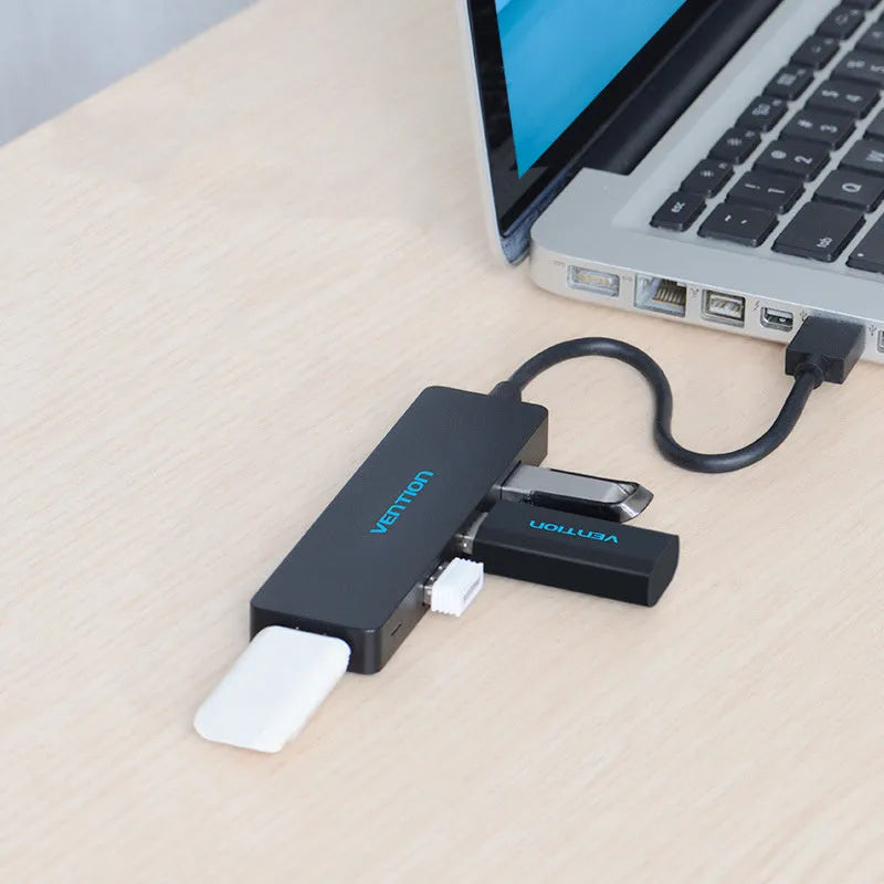 Black Wei Xun four-port USB 3.0 hub with short 15cm cable on a desk next to a laptop.
