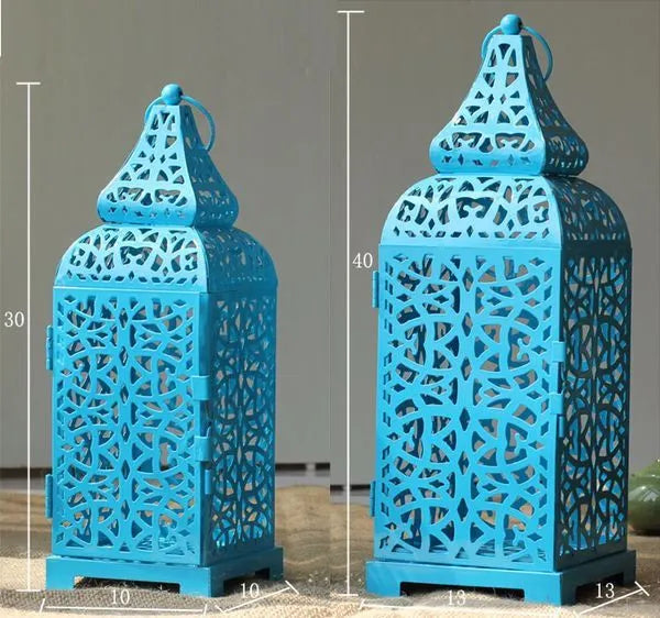 Blue iron geometric Moroccan candelabra holding a lit candle, with spare yellow and white taper candles beside it.