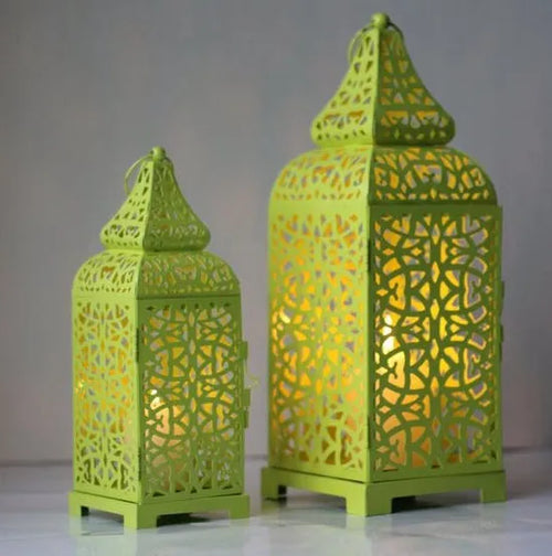 Blue iron geometric Moroccan candelabra holding a lit candle, with spare yellow and white taper candles beside it.