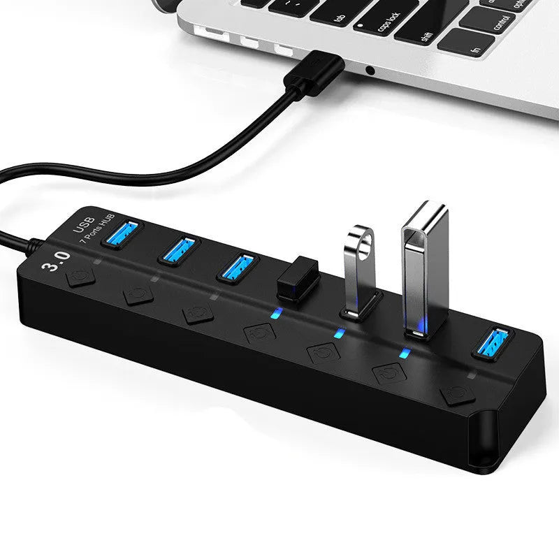 Black 7-port USB 3.0 hub with external power adapter and individual switches for each port on a desk.