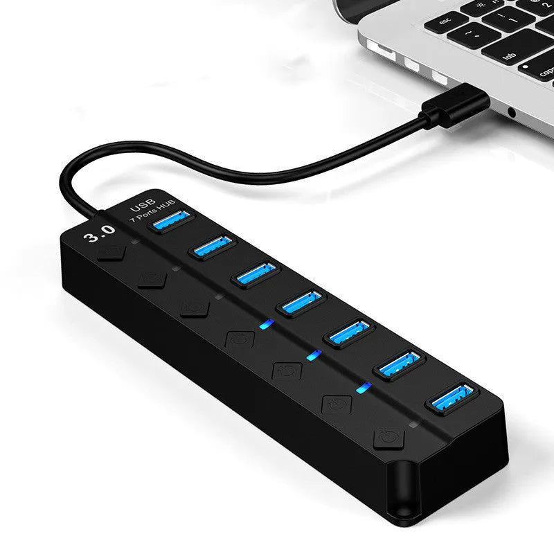 Black 7-port USB 3.0 hub with external power adapter and individual switches for each port on a desk.
