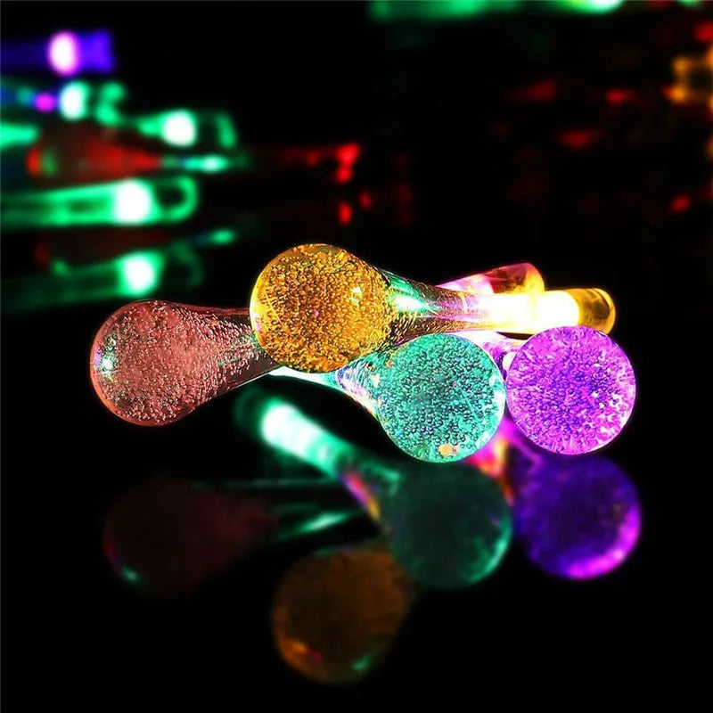 Solar-powered waterproof LED string lights with bubble drop pendants illuminating an outdoor garden space at dusk.