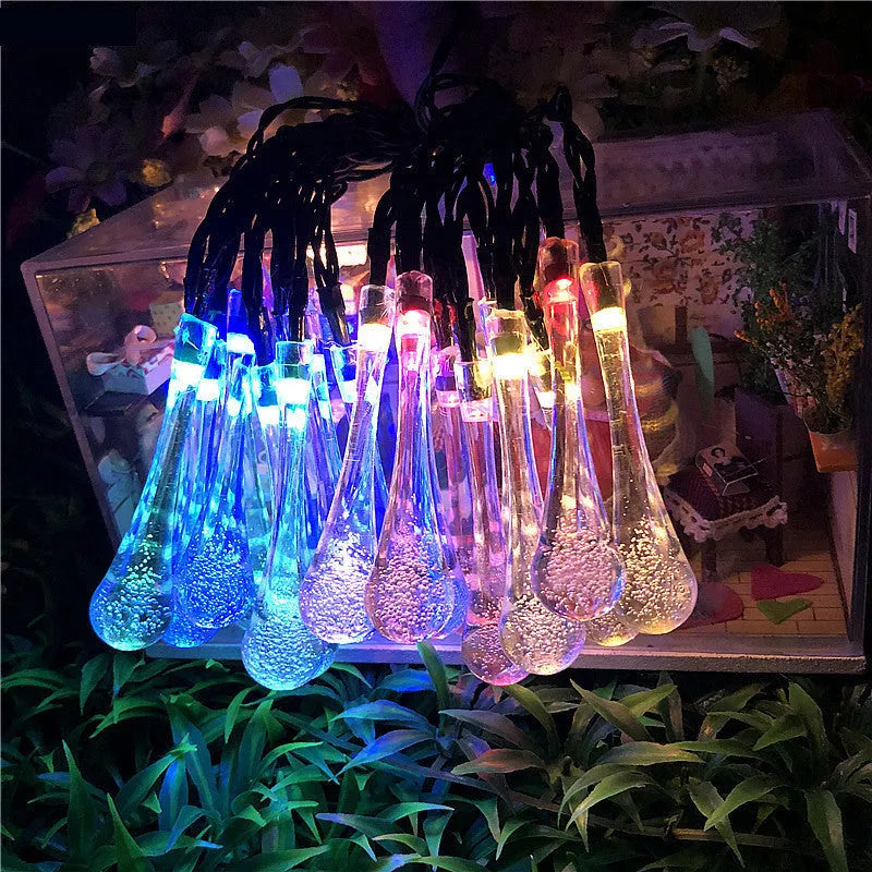 Solar-powered waterproof LED string lights with bubble drop pendants illuminating an outdoor garden space at dusk.