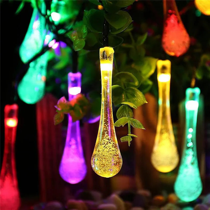 Solar-powered waterproof LED string lights with bubble drop pendants illuminating an outdoor garden space at dusk.