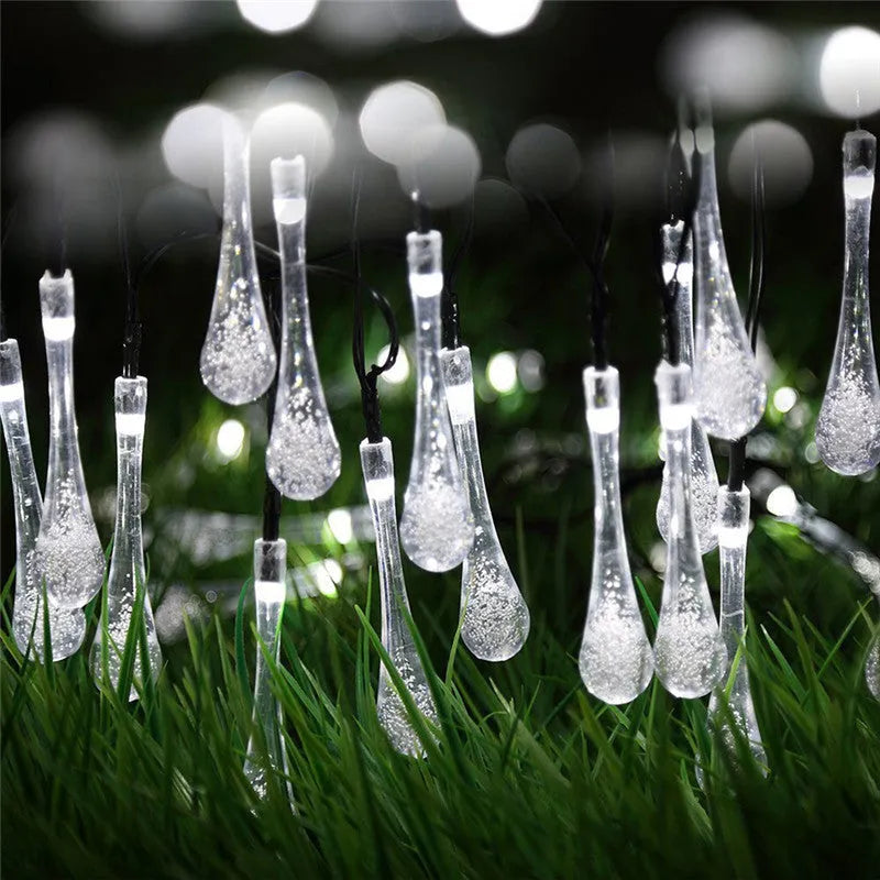 Solar-powered waterproof LED string lights with bubble drop pendants illuminating an outdoor garden space at dusk.
