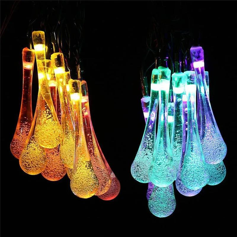 Solar-powered waterproof LED string lights with bubble drop pendants illuminating an outdoor garden space at dusk.