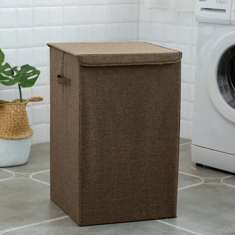 Washable fabric laundry sorting box in beige, shown next to a small pile of towels.