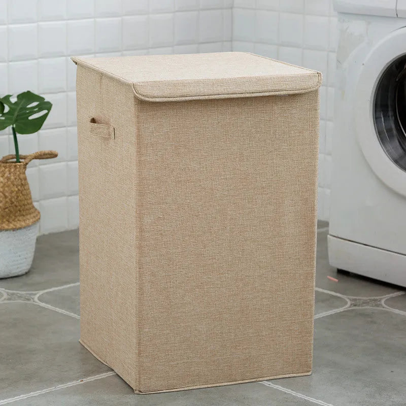Washable fabric laundry sorting box in beige, shown next to a small pile of towels.