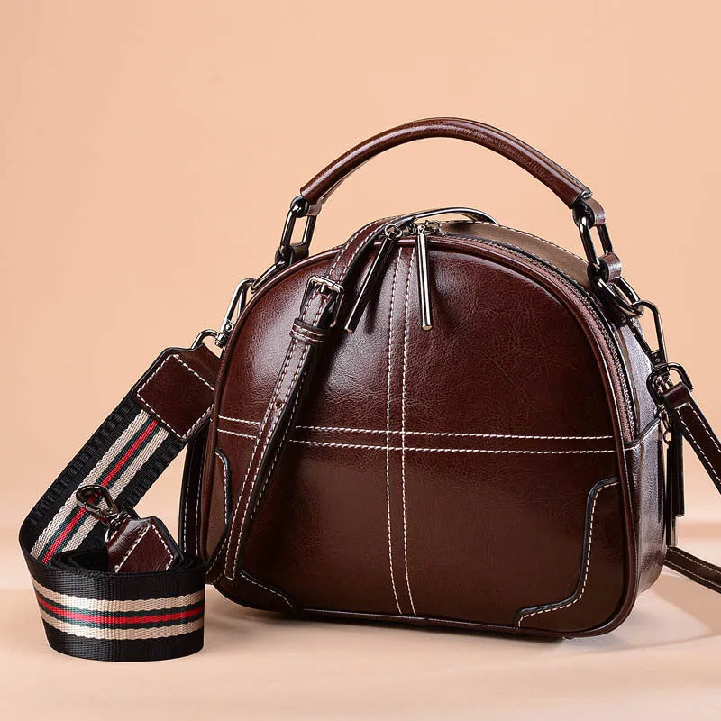 Round leather handbag with a zipper opening and a soft handle in a wine red colour.