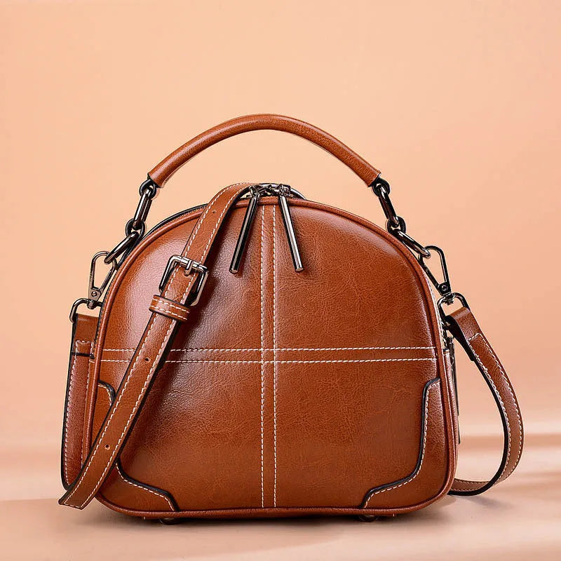 Round leather handbag with a zipper opening and a soft handle in a wine red colour.