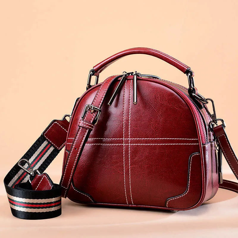 Round leather handbag with a zipper opening and a soft handle in a wine red colour.