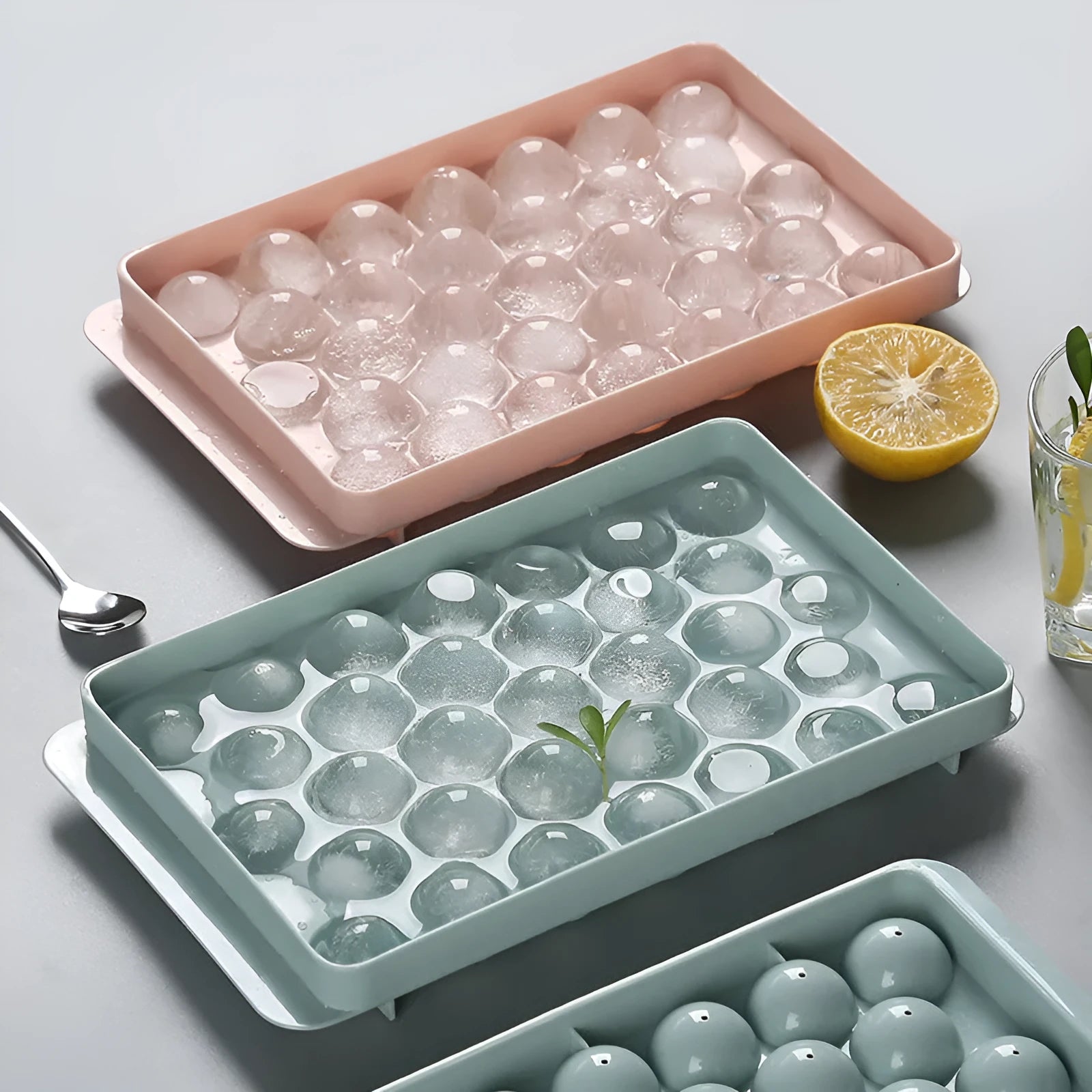 Sky blue 3D round ice ball mould tray with 18 grids next to a pink tray with 33 grids.