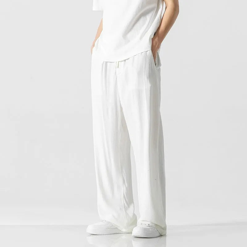 Man wearing beige straight-leg cropped bamboo fibre trousers with a drawstring waist on a summer day.