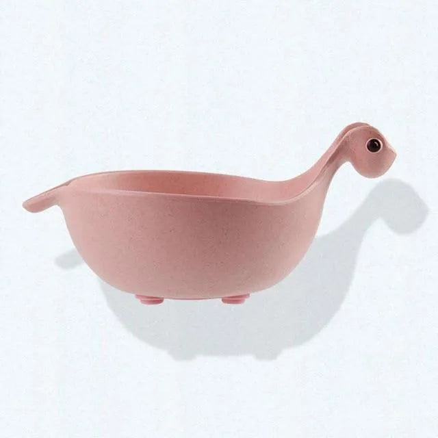 Three wheat straw dinosaur bowls in pink, green, and beige on a kitchen table