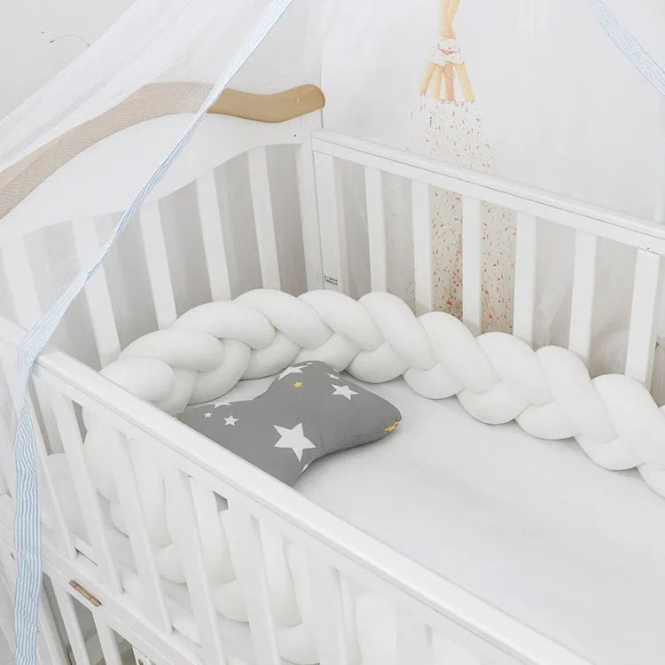 Close-up of a grey braid knot pillow cushion cot bumper fitted around white crib rails.