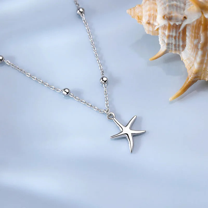 Close-up of a sterling silver anklet with round beads, a starfish charm, and an extender chain on an ankle.