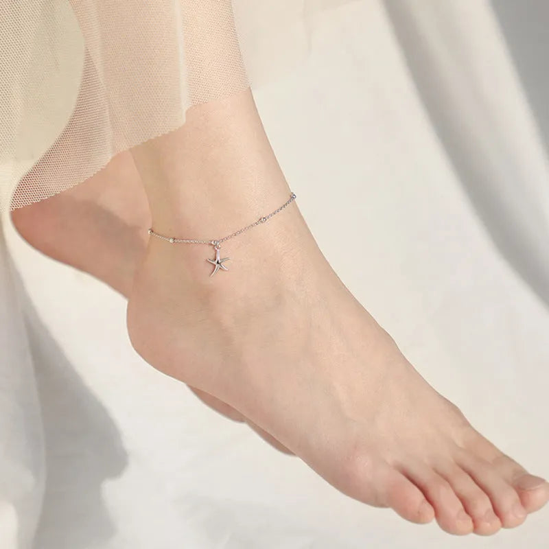 Close-up of a sterling silver anklet with round beads, a starfish charm, and an extender chain on an ankle.