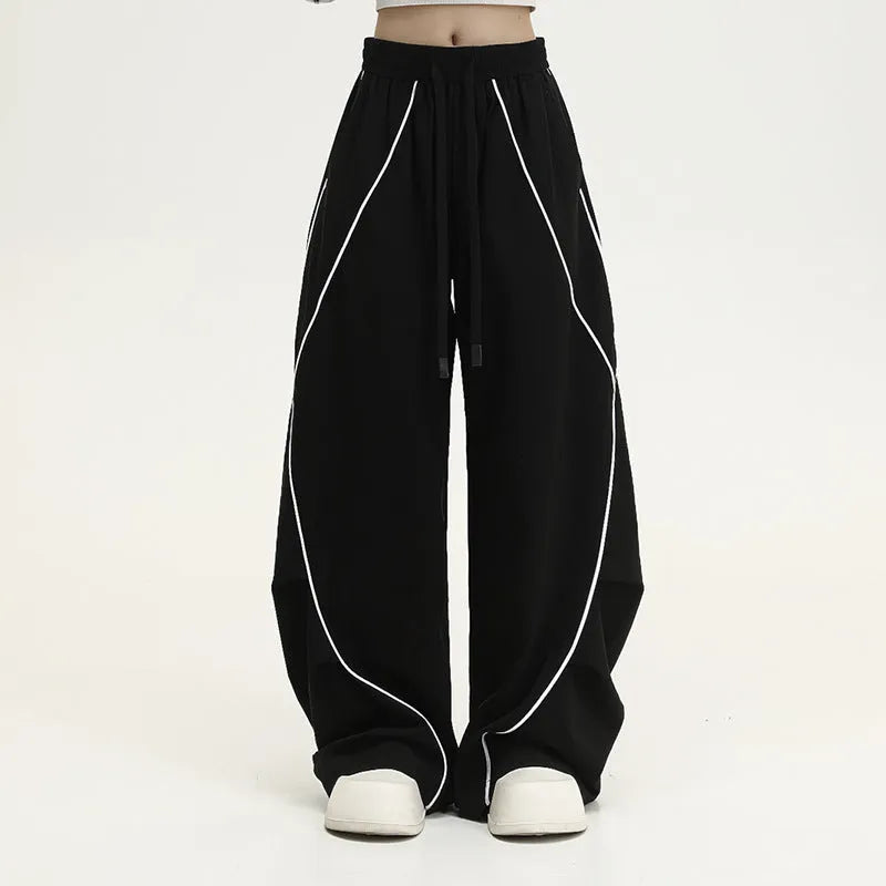 Black sports trousers with white stripes, showing wide-leg loose fit and mid-waist design.