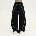 Black sports trousers with white stripes, showing wide-leg loose fit and mid-waist design.
