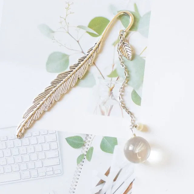 Flat metal bookmark with dried flower inside, showing 12cm length, on an open book.