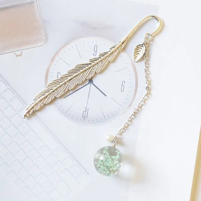 Flat metal bookmark with dried flower inside, showing 12cm length, on an open book.
