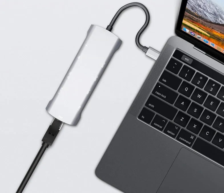Grey aluminium USB-C docking station with HDMI, VGA, USB 3.0, and PD charge ports on a desk.